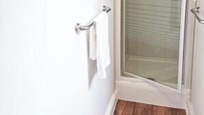 Une salle de bain avec une douche à parois de verre, une serviette blanche suspendue à un porte-serviettes en métal et un plancher en bois.
