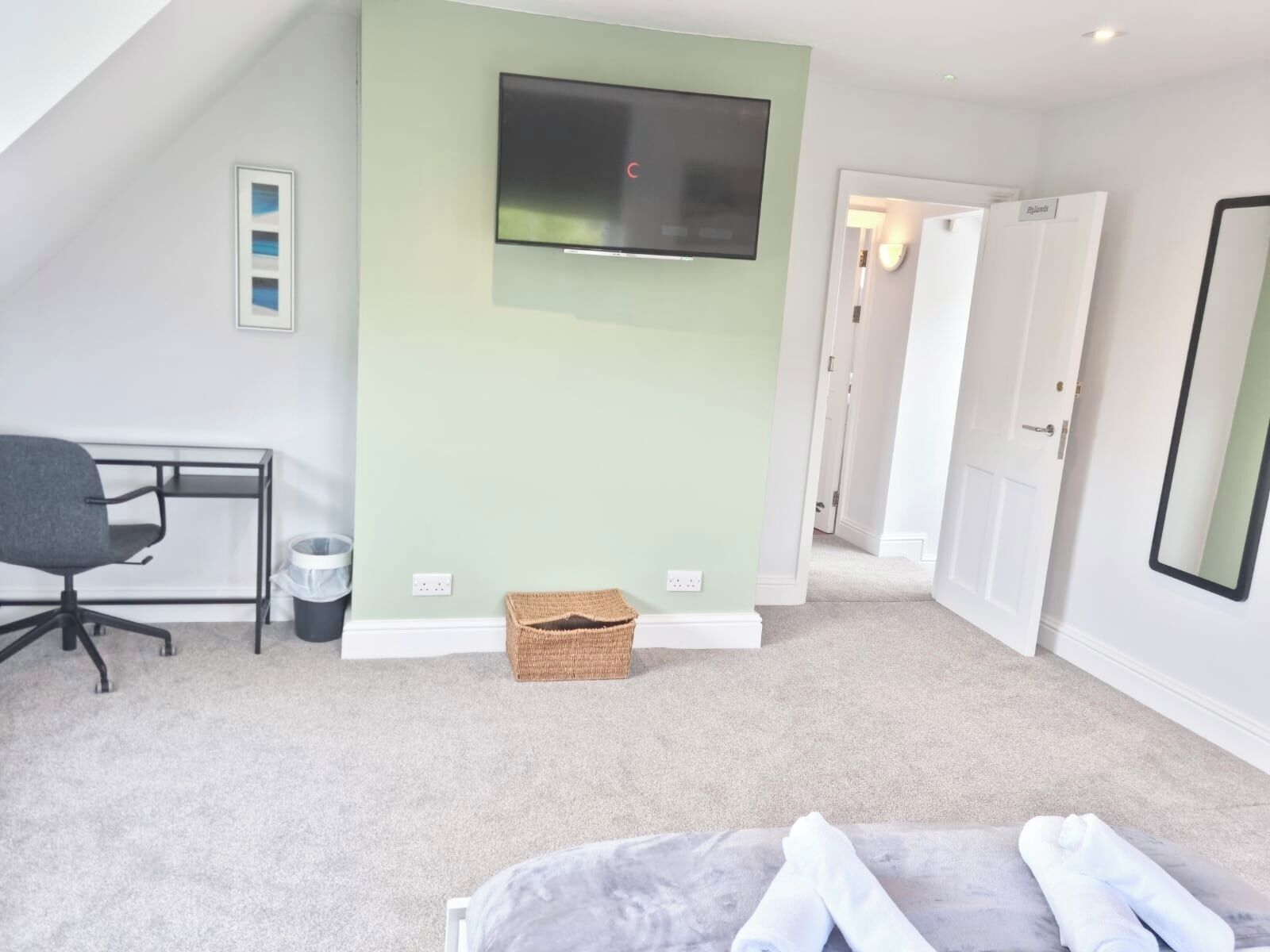 Une chambre à coucher comprenant un lit, un bureau, une chaise, un téléviseur et une porte donnant sur une autre pièce.