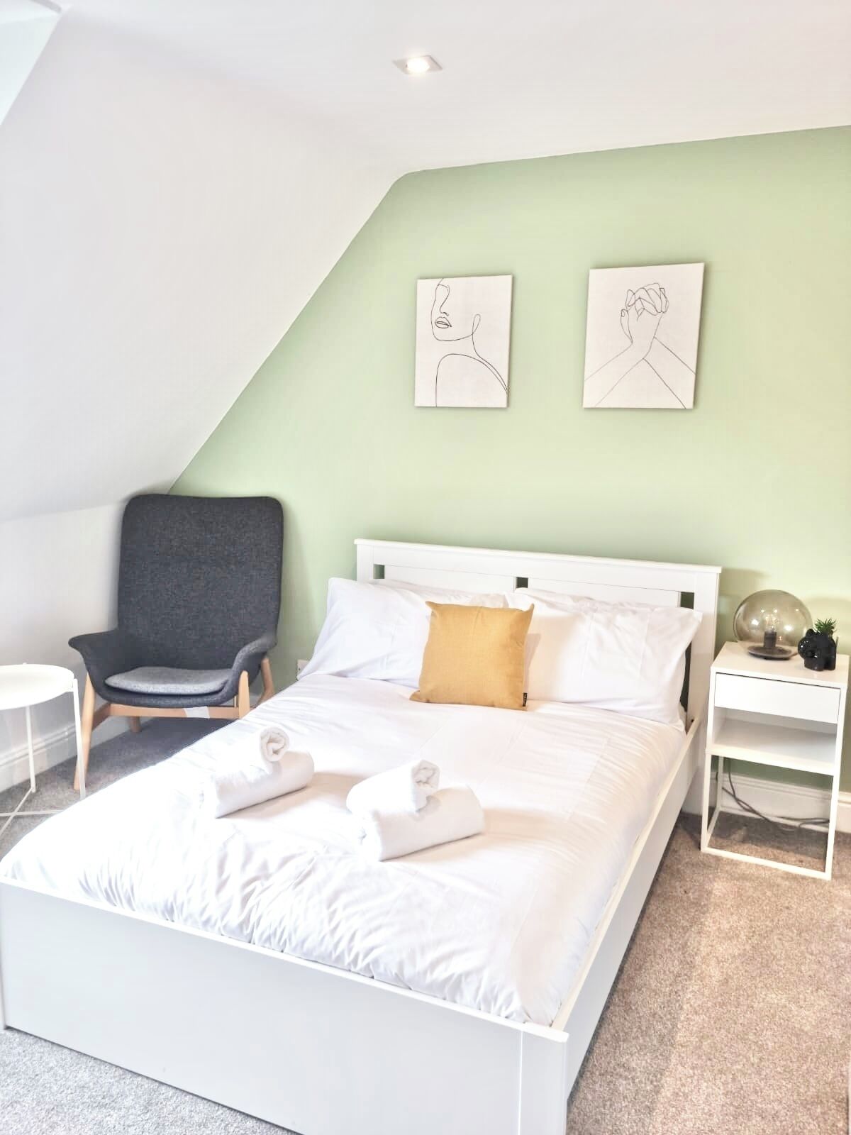 Un dormitorio moderno con una cama blanca, un sillón gris y dos obras de arte en la pared.