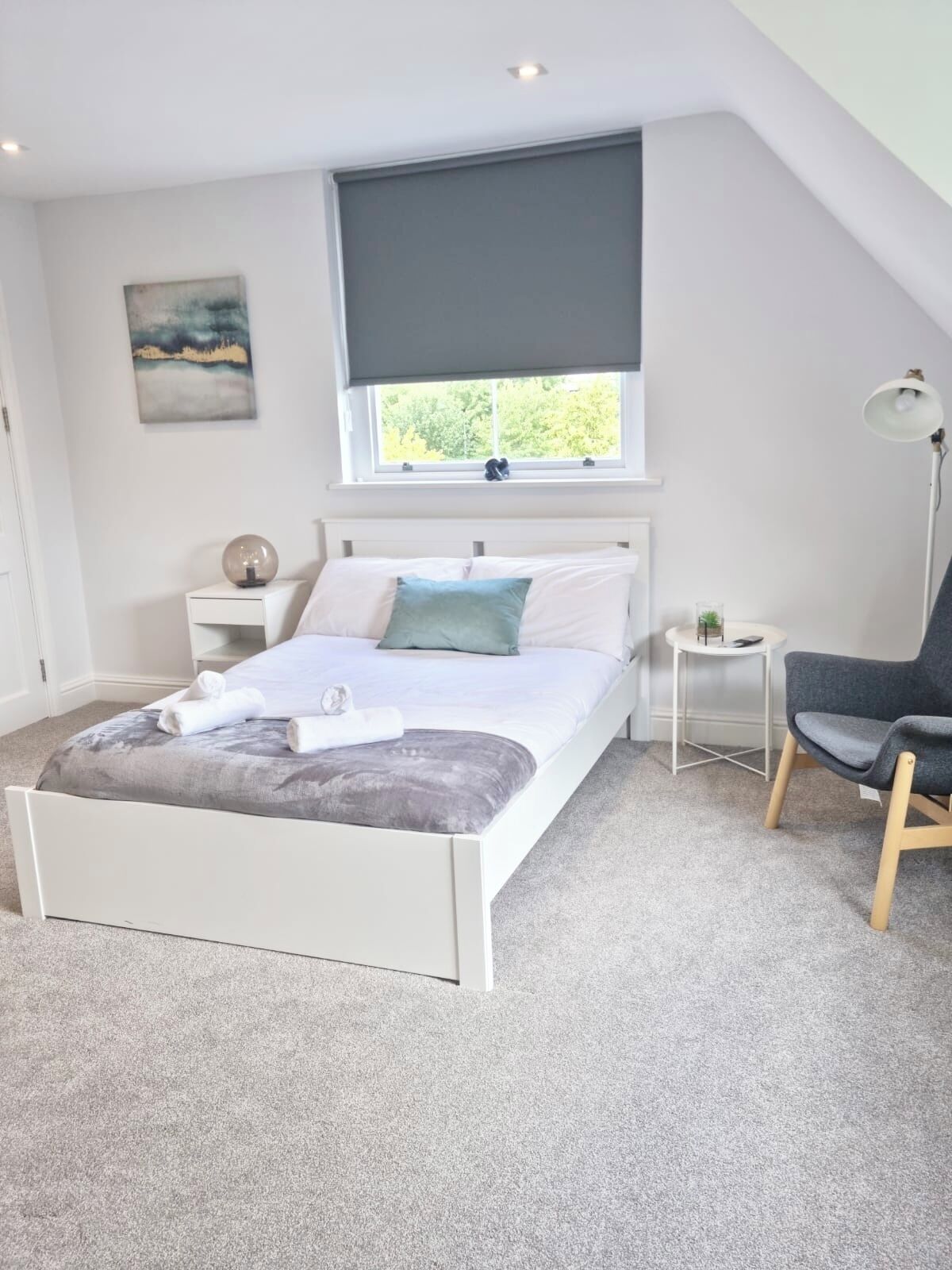 A bedroom with a bed, a bedside table, a lamp, a chair, and a window with a view of trees.