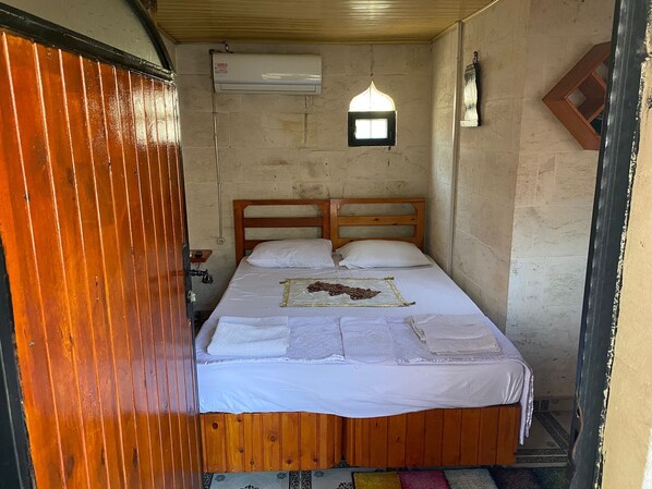 A small, rustic room with a wooden bed, a small window, and a wall-mounted air conditioner.