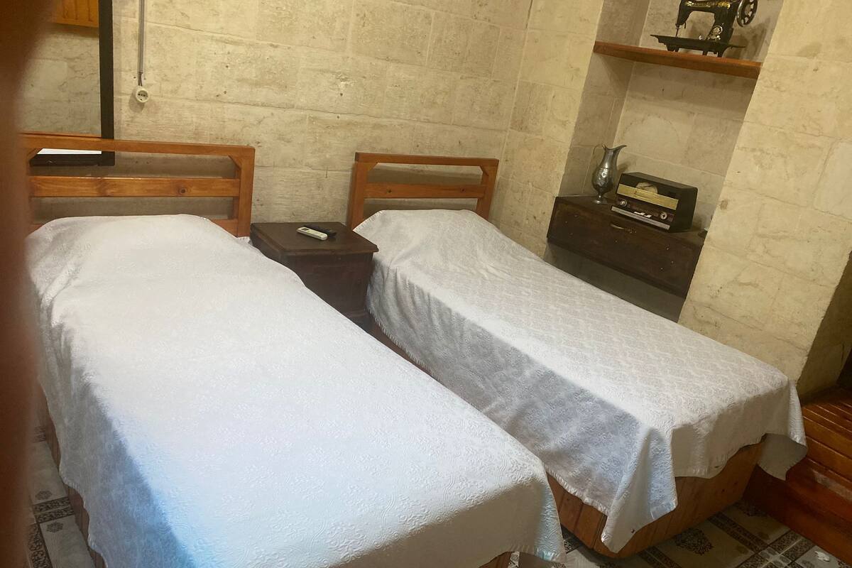 A room with two single beds, a wooden nightstand with a radio, and a brick wall.