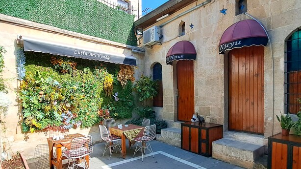 A courtyard with a table and chairs, a wooden cabinet, and a wall covered in greenery. - Lütfü Bey Konağı (Gaziantep)