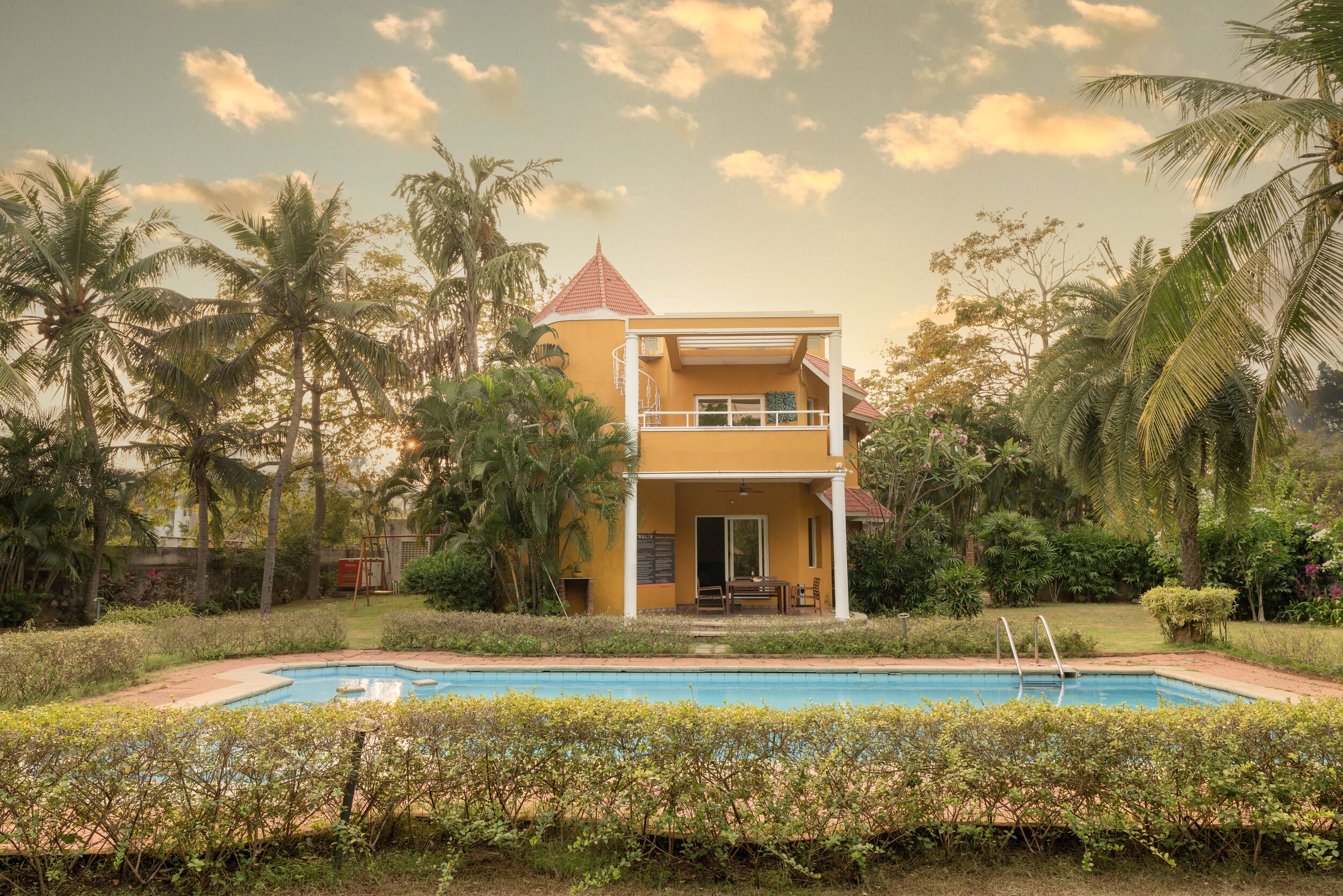 Un bâtiment à deux étages avec une piscine devant, entouré de palmiers et de verdure.