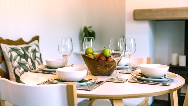 Una mesa de comedor con un frutero, copas de vino y cuencos blancos.