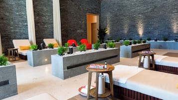 Un espacio moderno de spa con camillas de masaje, sillas rojas y macetas con plantas.