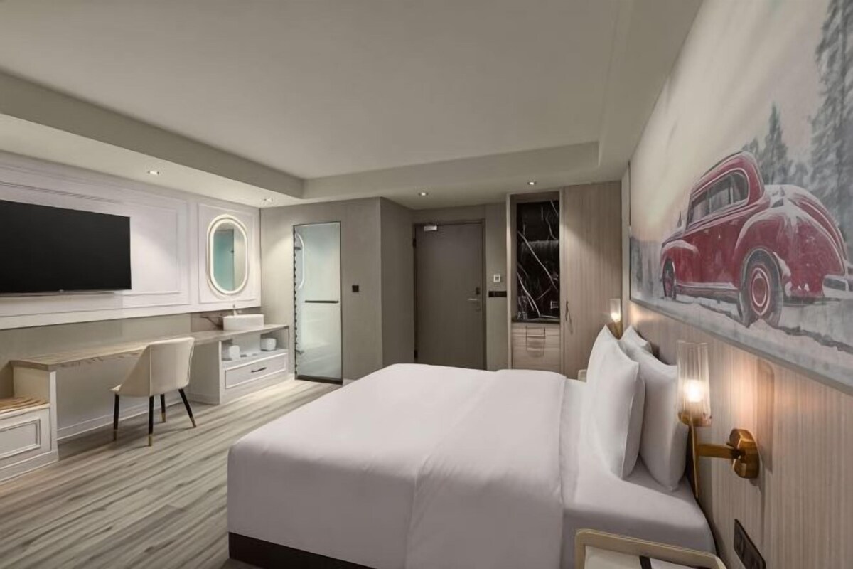 A modern hotel room with a large bed, a desk with a chair, a television, and a painting on the wall.