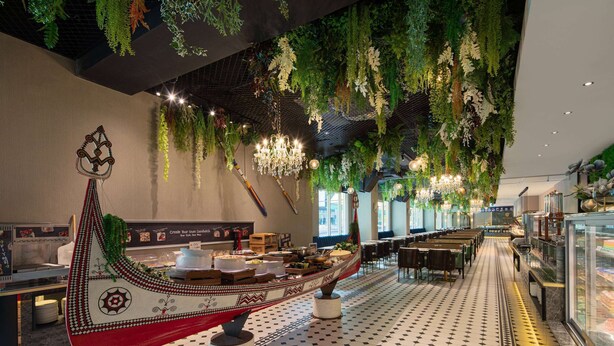 A restaurant with a long dining area, a decorative boat centerpiece, hanging plants, and a chandelier. - Tryp By Wyndham New Taipei Linkou (New Taipei City)