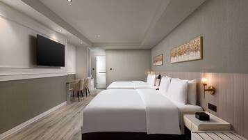 A hotel room with two beds, a flat-screen TV mounted on the wall, a desk with a chair, and artwork on the walls.