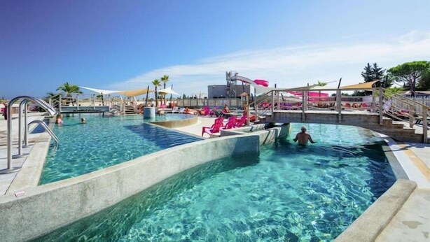 Una piscina de varios niveles con agua cristalina, rodeada de sillas de descanso y sombrillas.