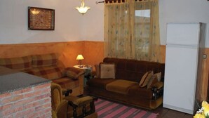 A living room with a brick fireplace, a sofa, a small table with a lamp, and a refrigerator. - Vivienda Vacacional EL Tazon (Cangas de Onís)