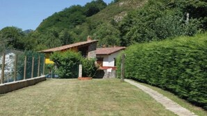 A house with a red roof, surrounded by a well-maintained lawn and dense greenery. - Vivienda Vacacional EL Tazon (Cangas de Onís)