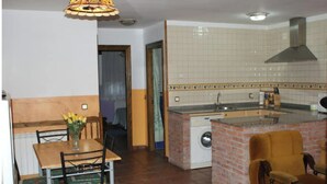 A compact kitchen with a washing machine, a dining area with a table and chairs, and a small island with a sink. - Vivienda Vacacional EL Tazon (Cangas de Onís)