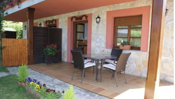 A covered patio with a stone wall, a wooden fence, and a table with chairs. - Vivienda Vacacional EL Tazon (Cangas de Onís)