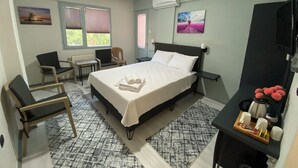A neatly arranged hotel room with a bed, two chairs, a small table, a desk, and a TV. - Eraliz (Izmir)