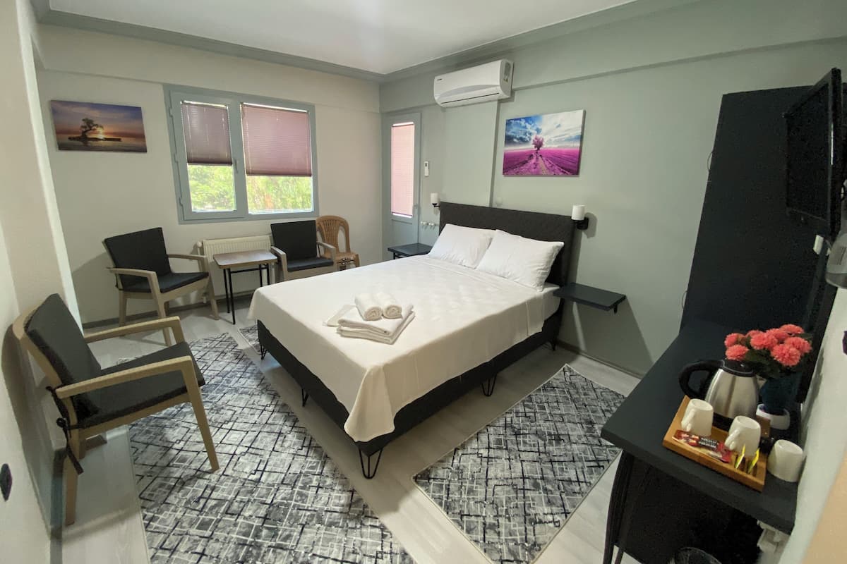 Ein ordentlich eingerichtetes Hotelzimmer mit einem Bett, zwei Stühlen, einem kleinen Tisch, einem Schreibtisch und einem Fernseher.