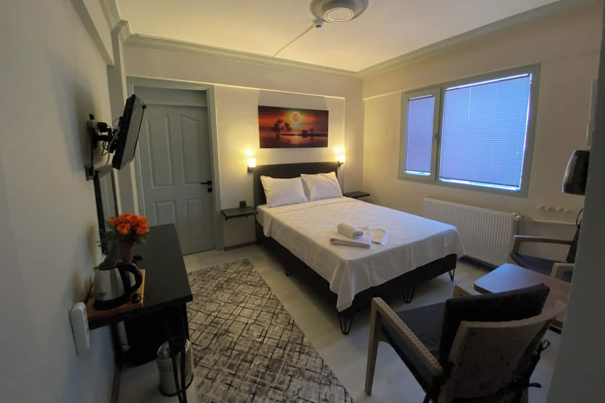 Ein Hotelzimmer mit Bett, Nachttisch, Lampe, Stuhl und einem Fenster mit Jalousien.