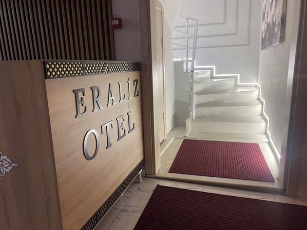 Entrada de un hotel con un letrero de madera que dice "ERALIZ HOTEL" y una escalera que sube a los pisos superiores.