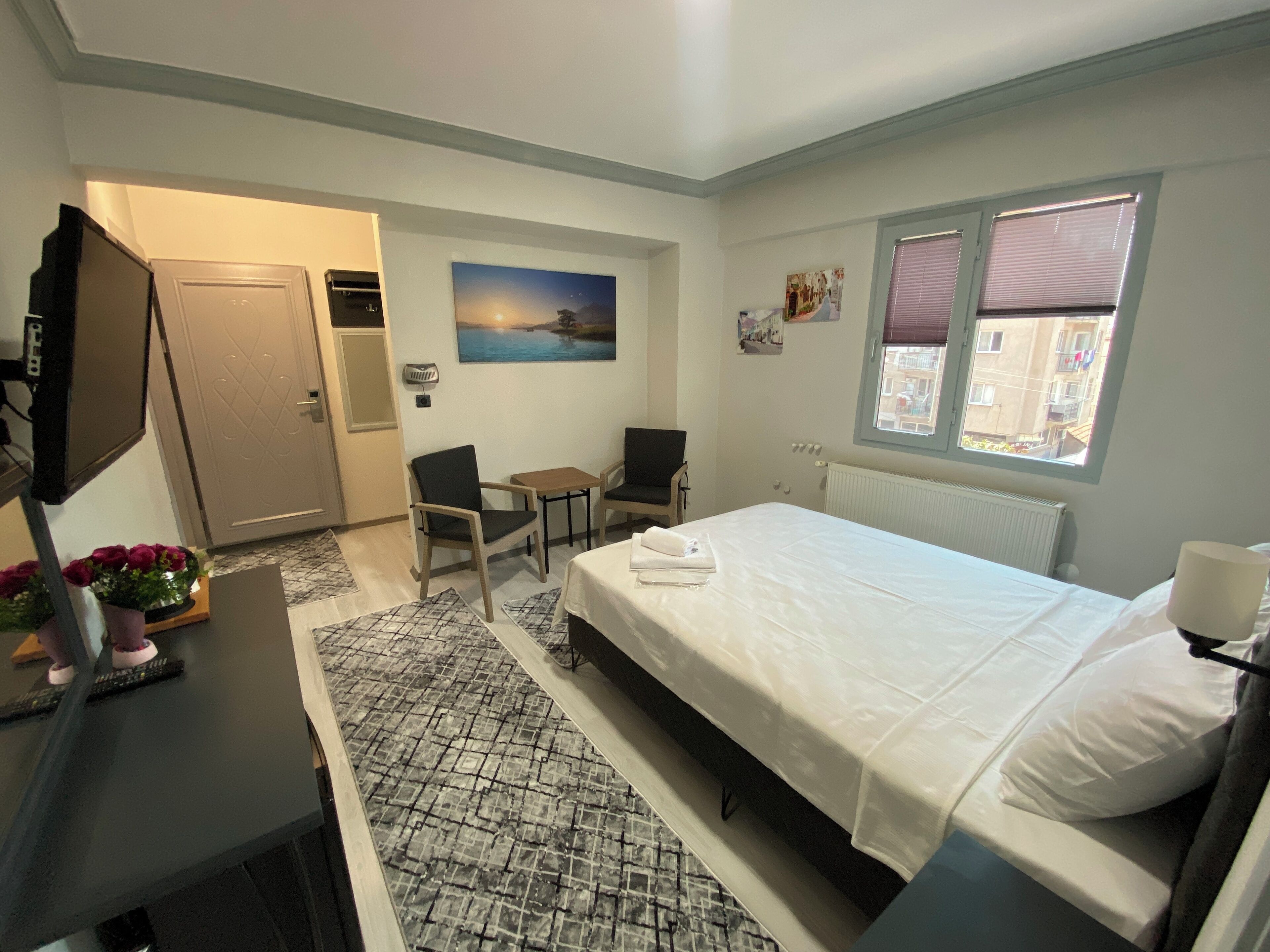 Quarto de hotel com cama, escrivaninha, cadeira, mesinha, televisão e janela com persianas.