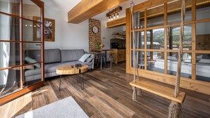 A modern living room with a wooden floor, a gray sofa, a wooden swing, and a large window with a view of a vehicle outside. - Korona Giewontu 3 (Koscielisko)