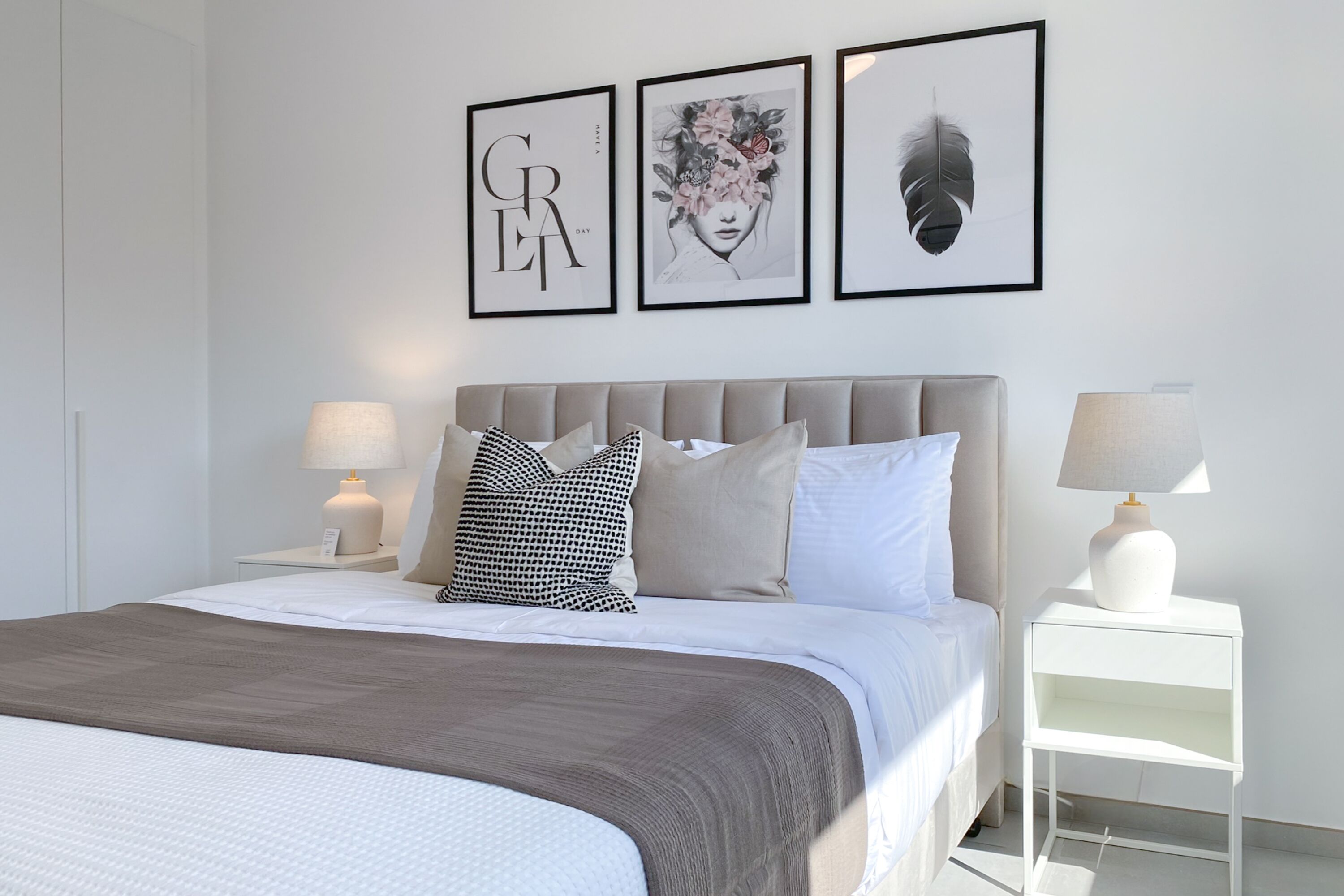A modern bedroom with a large bed, two bedside tables with lamps, and three framed artworks on the wall.