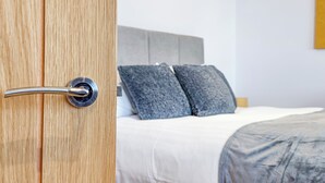 Ein Hotelzimmer mit Holztür, einem Bett mit grauer Bettwäsche und einem grauen Kopfteil.
