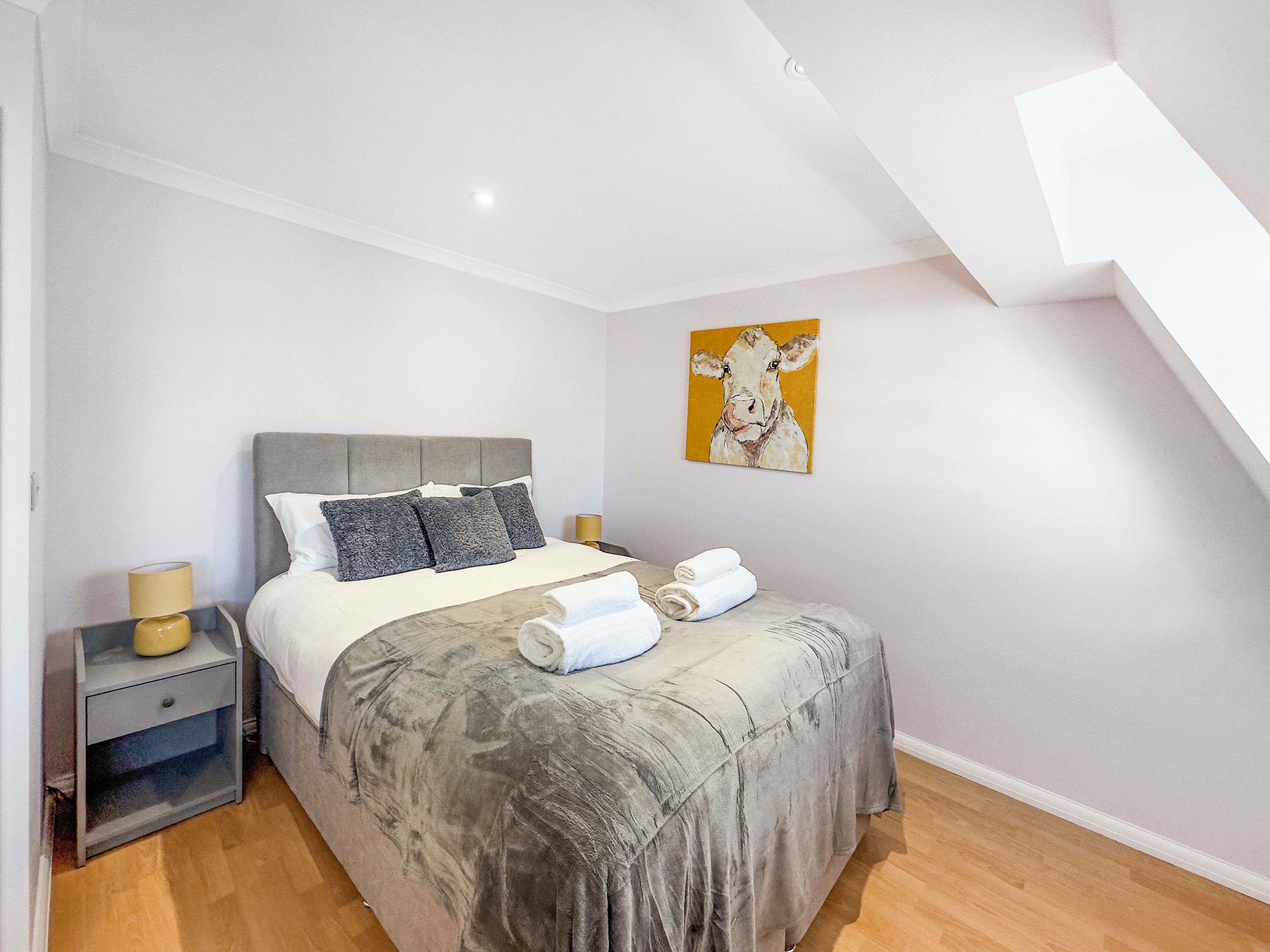 A bedroom with a bed, a nightstand, a lamp, and a painting on the wall.