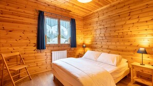 A wooden cabin bedroom with a bed, two nightstands, a chair, and a window with curtains. - Chalet les deux marmottes - Vue montagne (Bolquère)