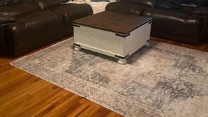 Un soggiorno con un divano in pelle marrone scuro, un tavolino da caffè bianco e un tappeto decorato su un pavimento in legno.