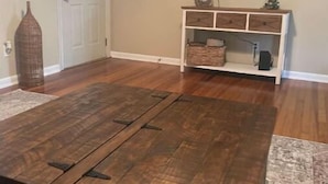 Una stanza con pavimento in legno, TV a parete, una porta bianca e un piccolo tavolo consolle bianco con cassetti.