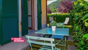 An outdoor patio with a table and chairs, a potted plant, and a view of a hillside. - Infinity Apartment by Wonderful Italy (Bellagio)