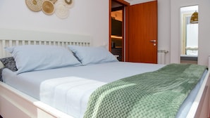 A neatly made bed with a white headboard and a green blanket, a wooden door, and a wall with woven wall art. - Infinity Apartment by Wonderful Italy (Bellagio)