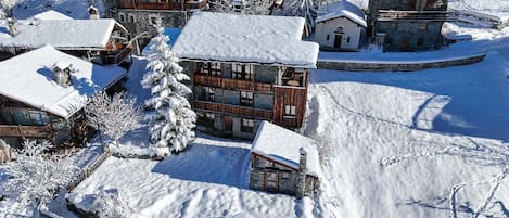 Un pueblo cubierto de nieve con cabañas de madera y un edificio de piedra, rodeado de árboles nevados y un lago congelado.