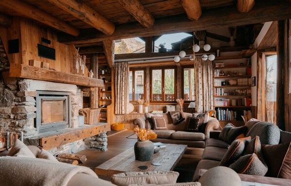 A cozy log cabin interior with a stone fireplace, a large sofa, and a bookshelf filled with books.