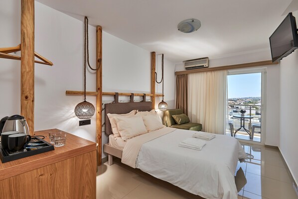 Une chambre d’hôtel avec un lit, une table de chevet en bois sur laquelle se trouvent une bouilloire et des verres, une lampe fixée au mur et une vue sur la ville par la fenêtre.