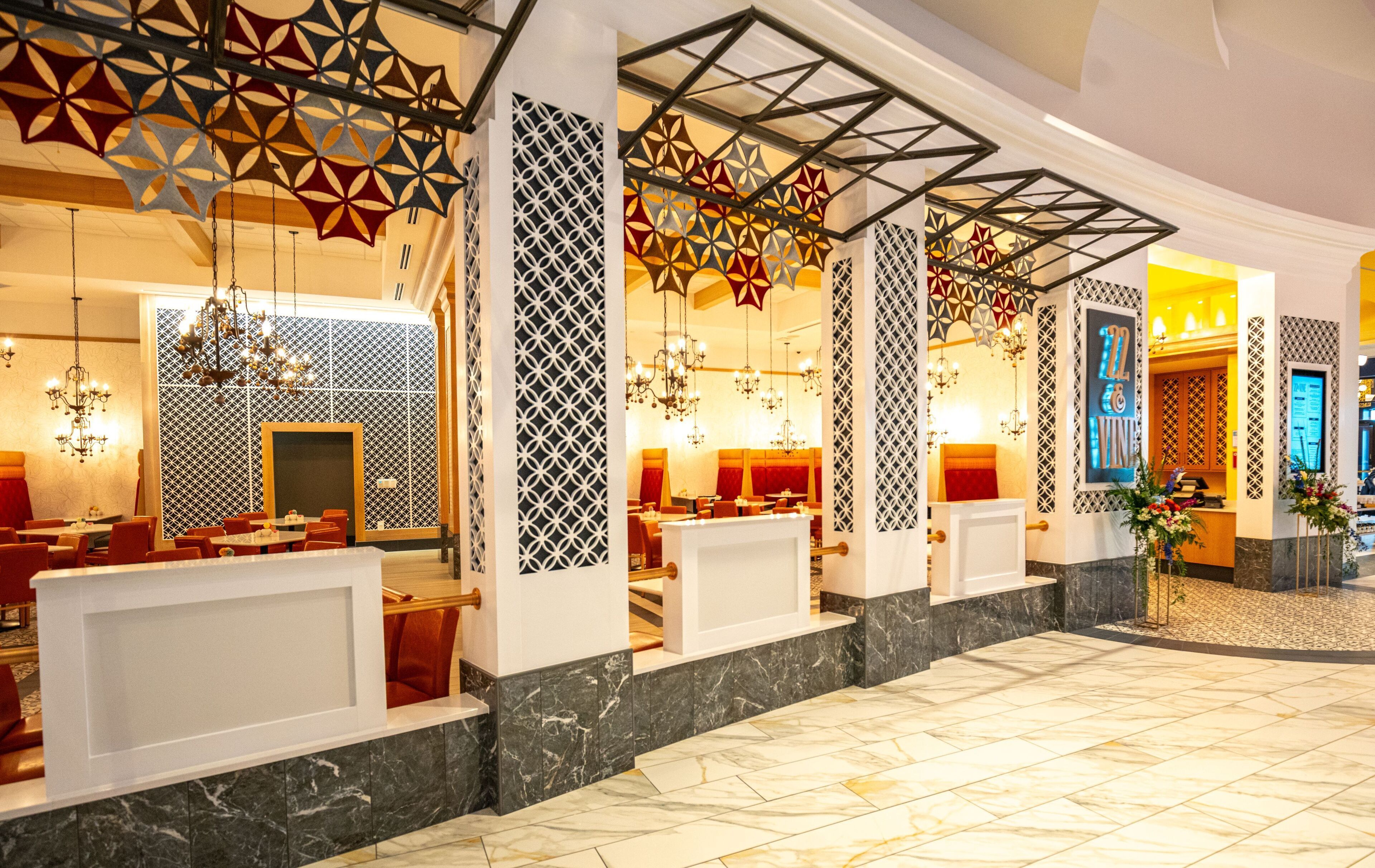 A hotel lobby with a modern design, featuring geometric patterned walls, chandeliers, and marble flooring.