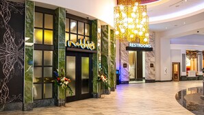 Een hotel lobby met een marmeren vloer, een receptiebalie, een bordje 'Toiletten' en een grote kroonluchter.