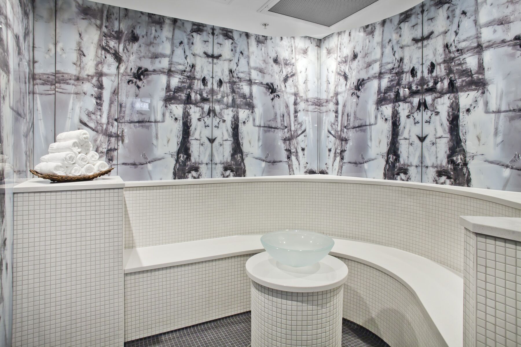 A modern bathroom with a large bathtub, a glass bowl sink, and a wall with a tree pattern.