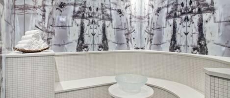 A modern bathroom with a large bathtub, a glass bowl sink, and a wall with a tree pattern.