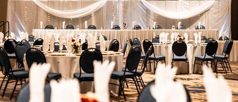 Un salón de banquetes con mesas redondas, sillas negras y manteles blancos.
