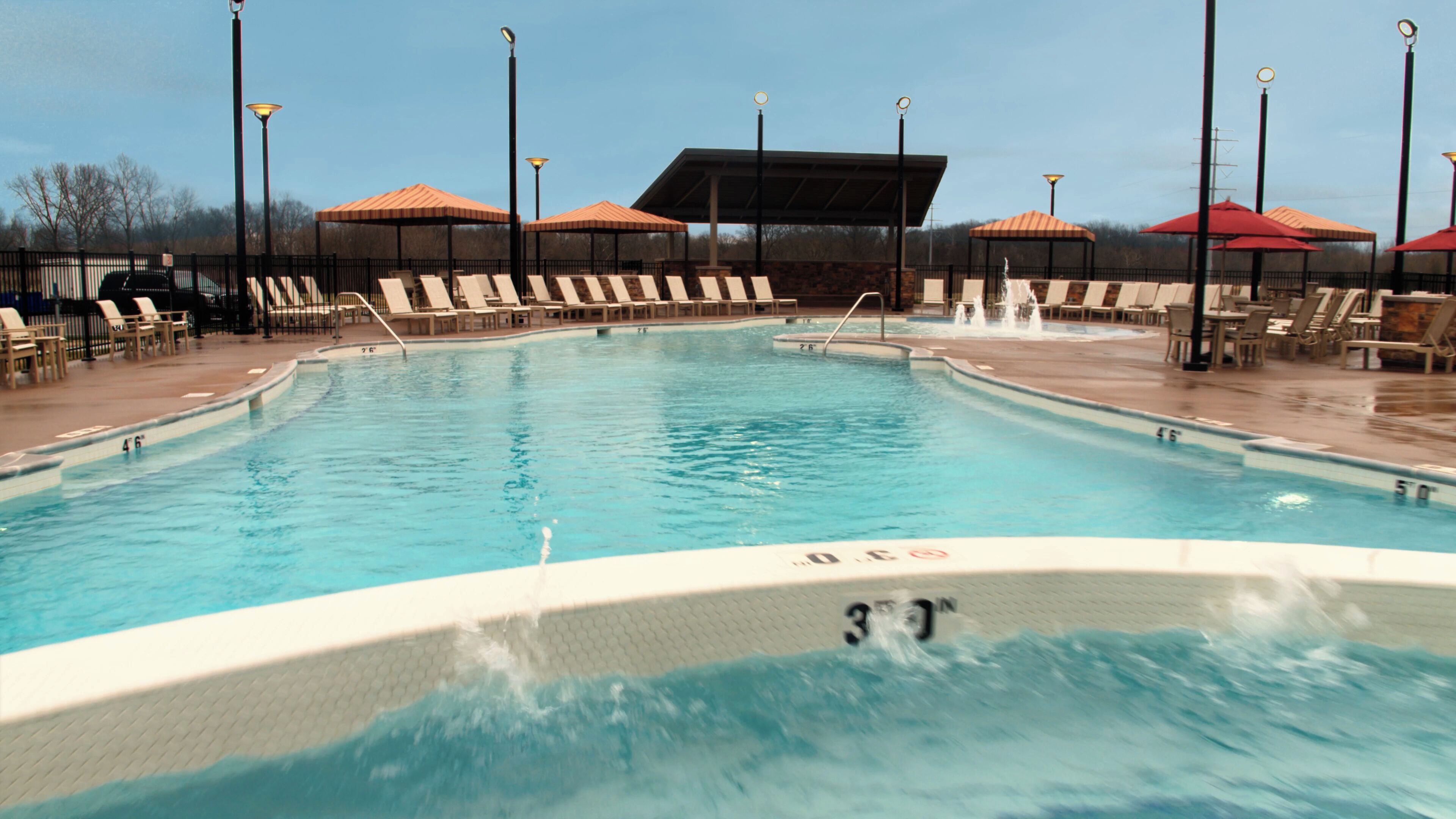 A swimming pool with lounge chairs and umbrellas, surrounded by a covered seating area.
