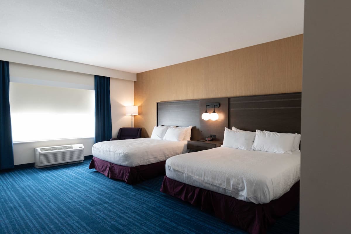 A hotel room with two beds, a desk, a chair, a lamp, and a window with curtains.