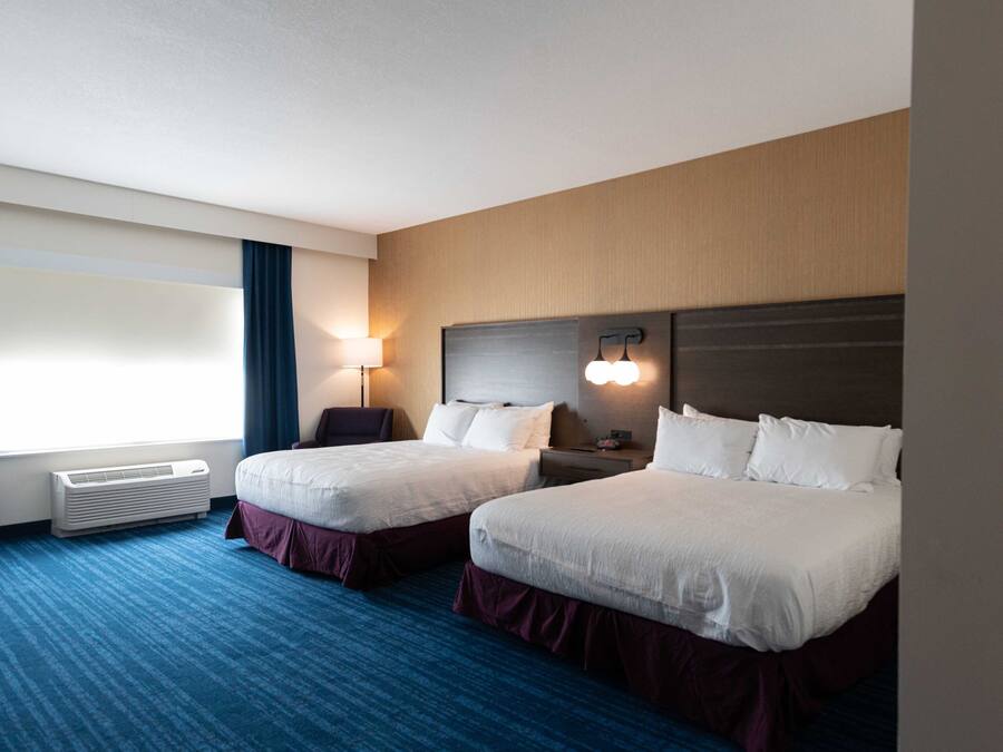 A hotel room with two beds, a desk, a chair, a lamp, and a window with curtains.