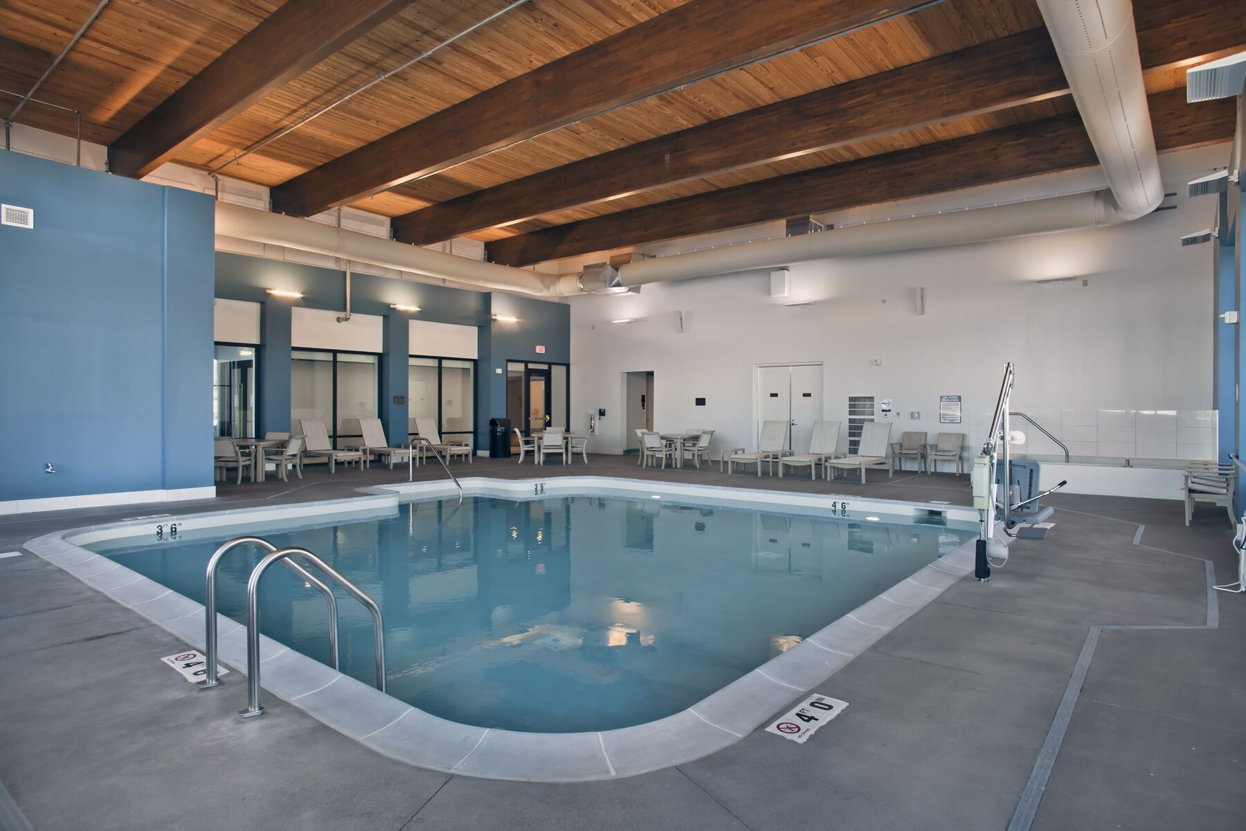 Une piscine intérieure avec des lignes de démarcation bien visibles, un poste de surveillance pour les sauveteurs et des chaises longues disposées autour de la piscine.