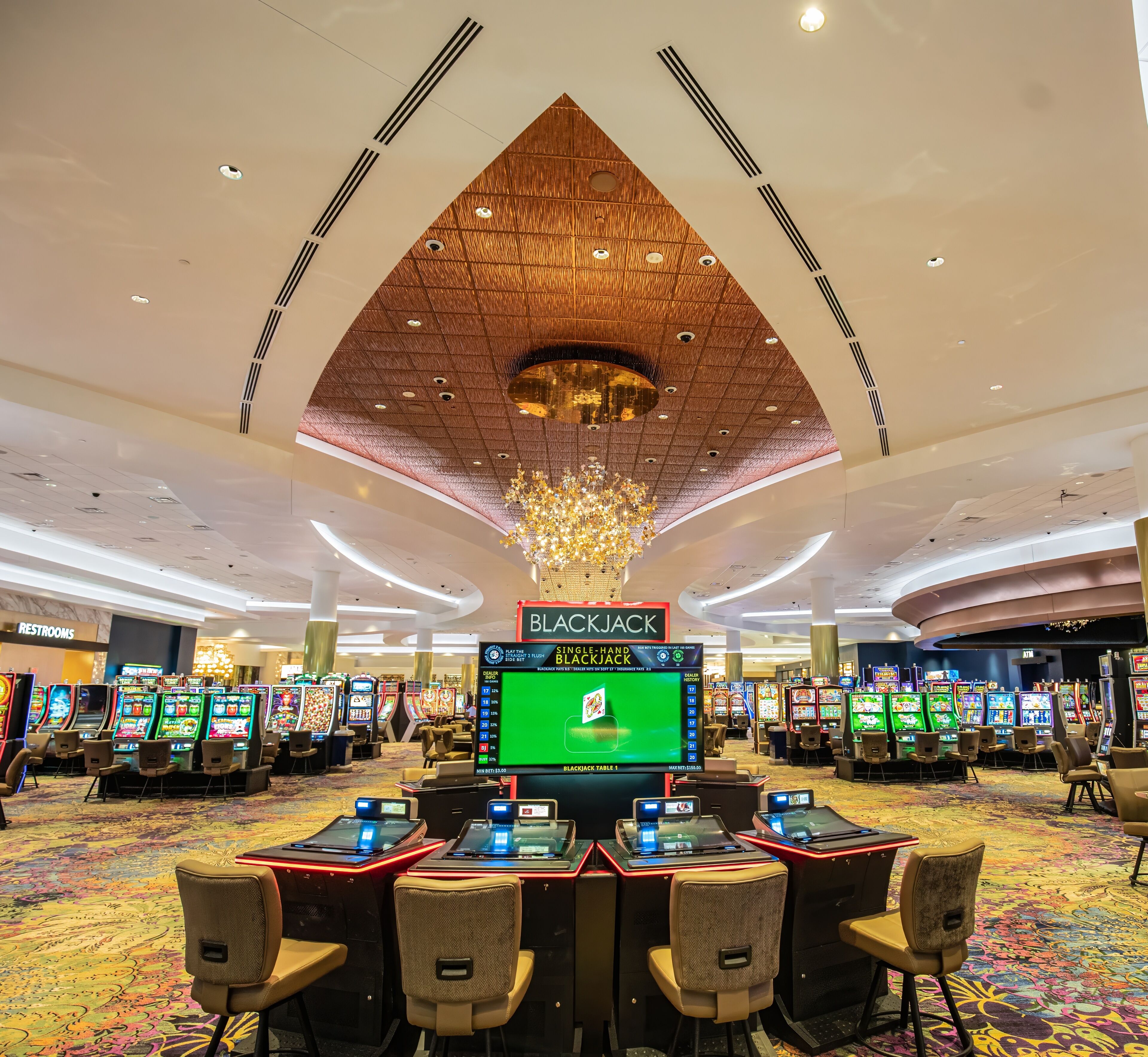 A casino area with blackjack tables, slot machines, and a large chandelier.