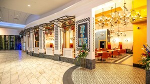 Een hotel lobby met een marmeren vloer, een receptie met een '12 & VINE' bord en een eetgedeelte met oranje stoelen en kroonluchters.