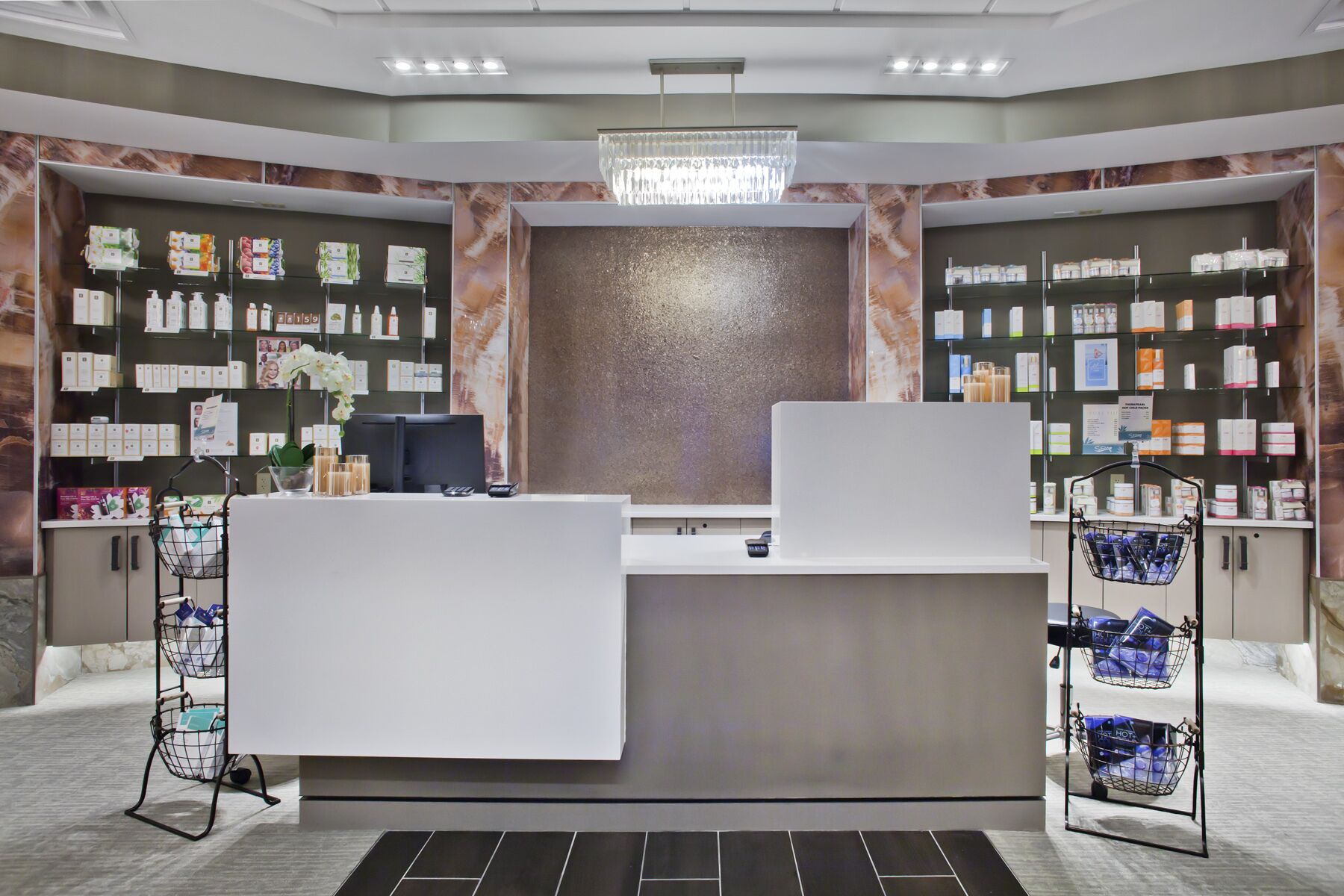 A hotel reception area with a modern design, featuring a reception desk, a large wall-mounted display, and shelves stocked with toiletries.