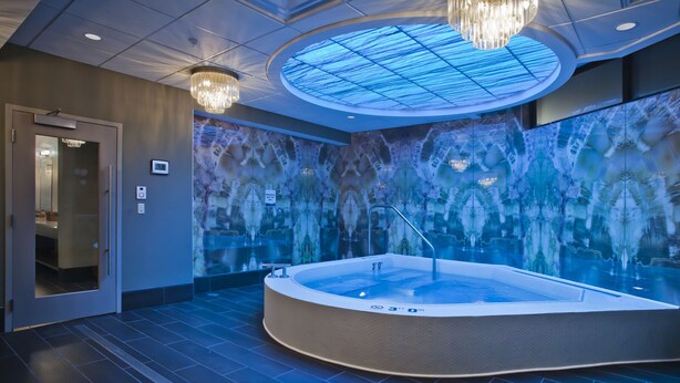 Een moderne spa ruimte met een ruime jacuzzi, een glazen wand met een reflecterend patroon en een plafond met een dakraam.