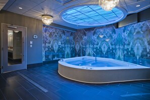 Un moderno spa con una bañera de hidromasaje grande, un muro de cristal con un diseño reflectante y un techo con tragaluces.