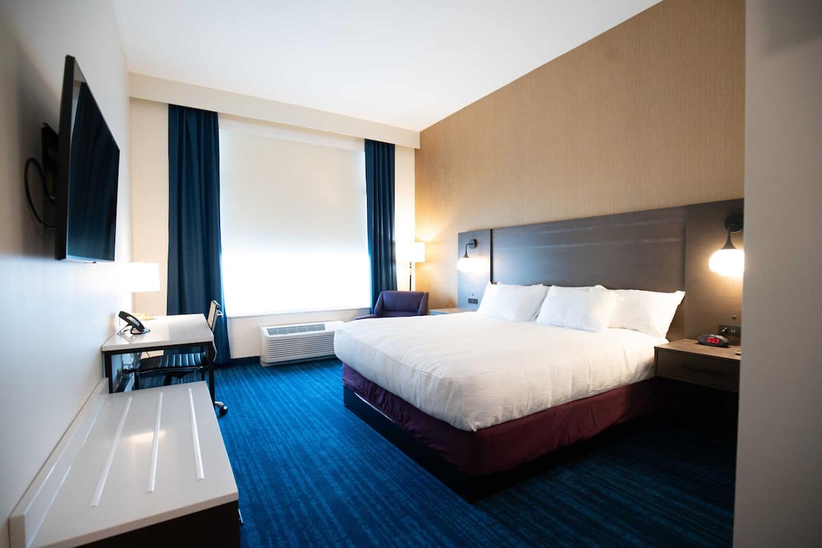 A hotel room with a bed, desk, chair, and a flat-screen TV mounted on the wall.